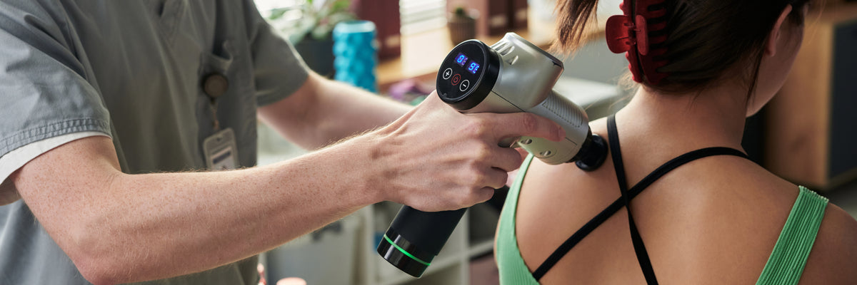 Therapist using a massage gun on a person's shoulder for muscle recovery